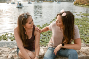Friend comforting another sitting by a lake with boats