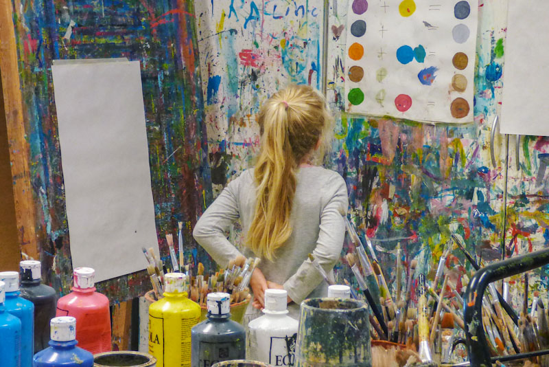 Woman with paintbrushes looking at color palette