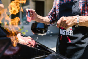 Man basting chops on a grill over a flame
