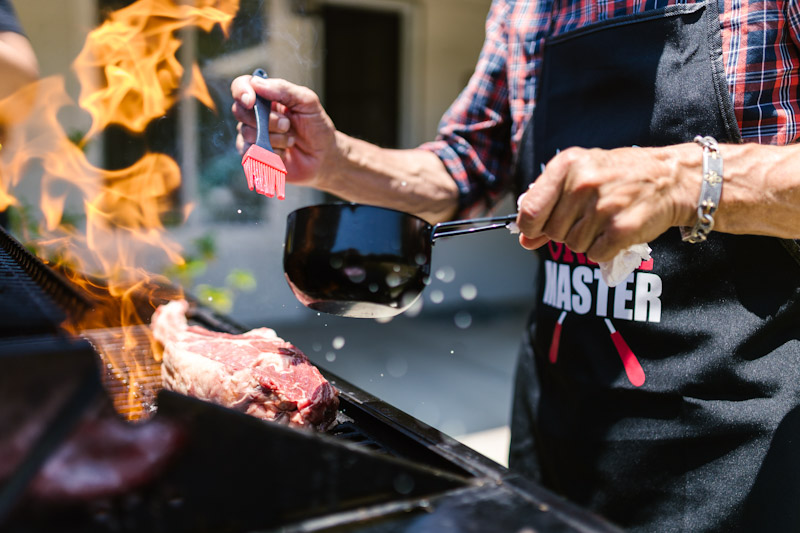 Man basting chops on a grill over a flame